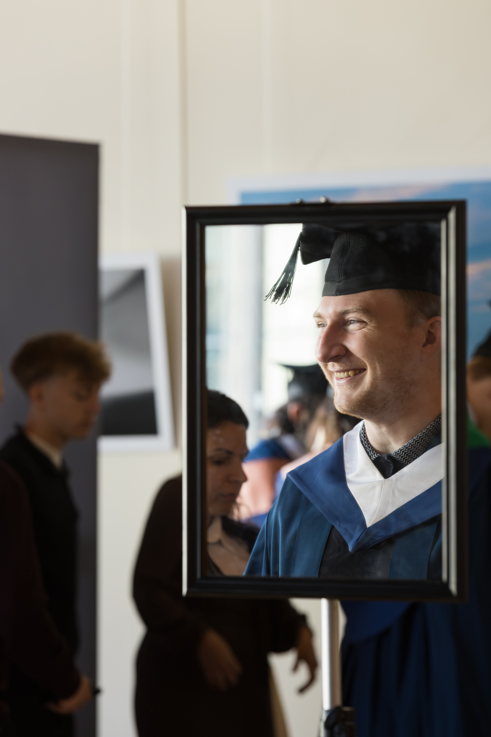 A graduate getting gowned up and smiling - picture of reliction in a mirror