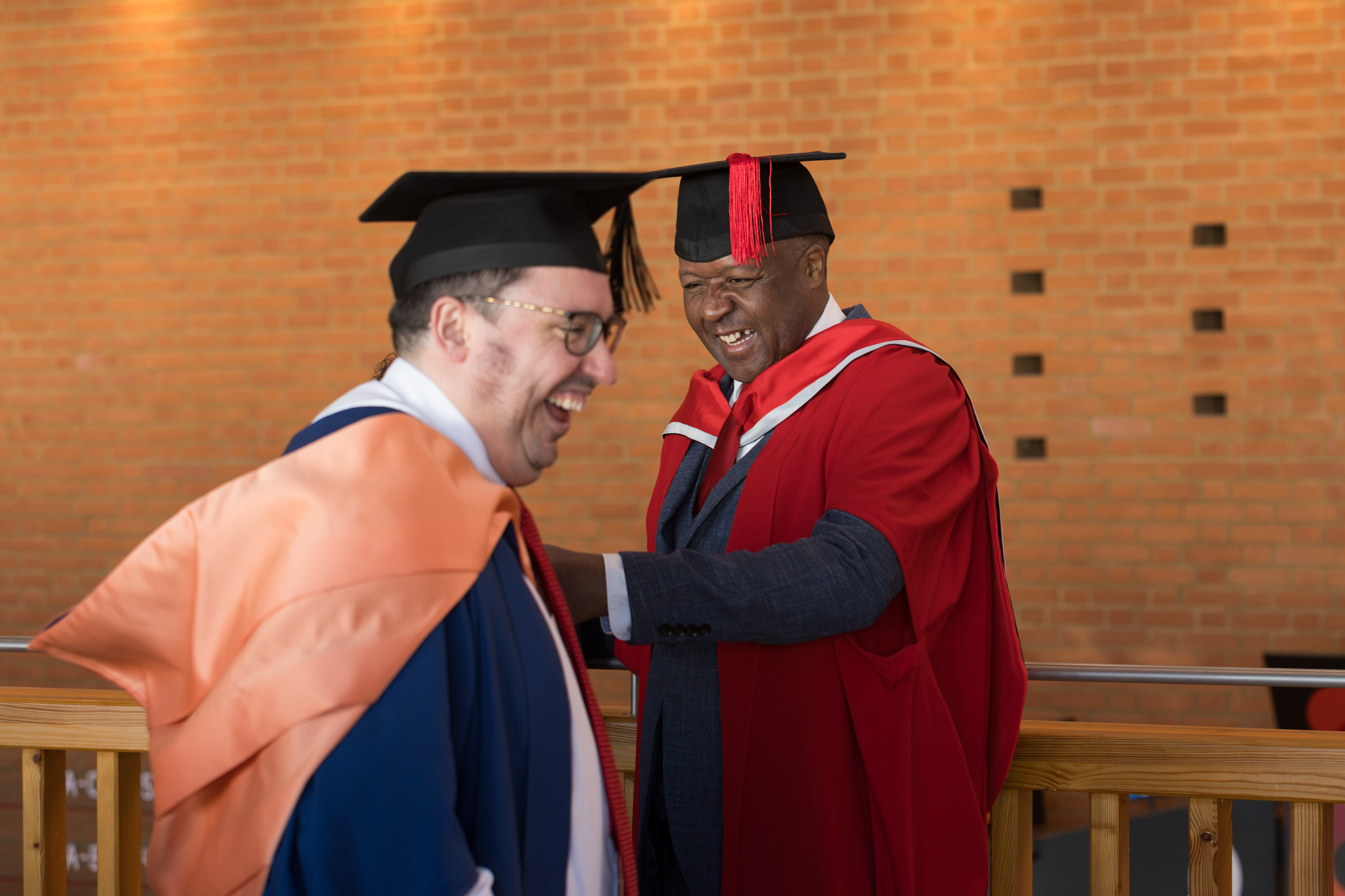 Two staff members laughing in their graduation costumes